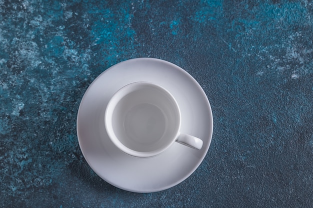 Tazza bianca vuota per caffè sul tavolo blu, vista dall'alto