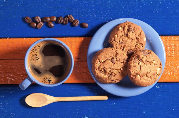 Tazza blu di caffè caldo con gustosi biscotti al cioccolato su tavolo in legno colorato vista dall'alto