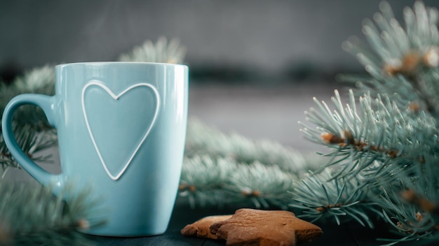 Tazza blu parzialmente sfocata con cuore con rami di albero di Natale e biscotti di pan di zenzero, spazio per copie.