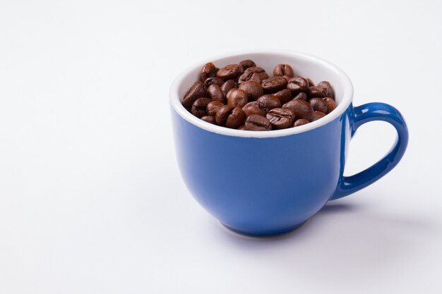 Tazza blu piena di chicchi di caffè isolati su bianco