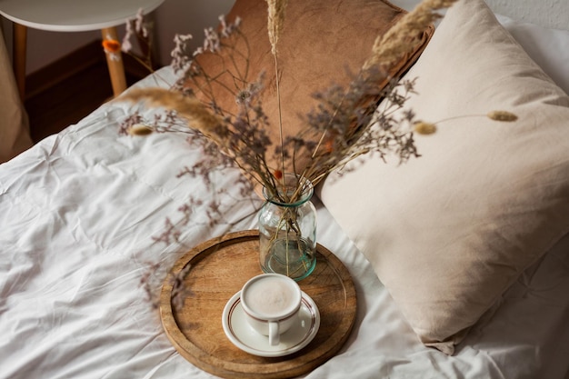 Tazza calda di cappuccino sul vassoio di legno sul letto colazione bouquet di fiori secchi Scenario primaverile Casa accogliente Colori naturali beige