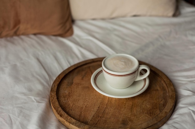 Tazza calda di cappuccino sul vassoio di legno sul letto colazione Casa accogliente Colori naturali beige Estetica