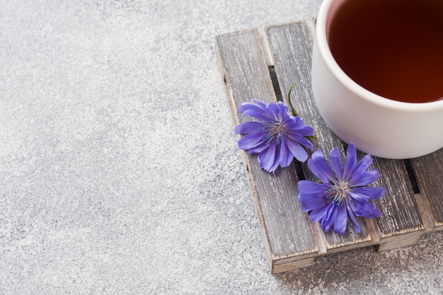 Tazza con bevanda di cicoria e fiori di cicoria blu sul tavolo grigio