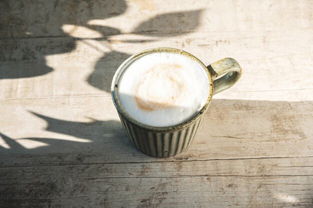 Tazza con caffè cappuccino su un legno bianco con un'ombra dalle foglie degli alberi.