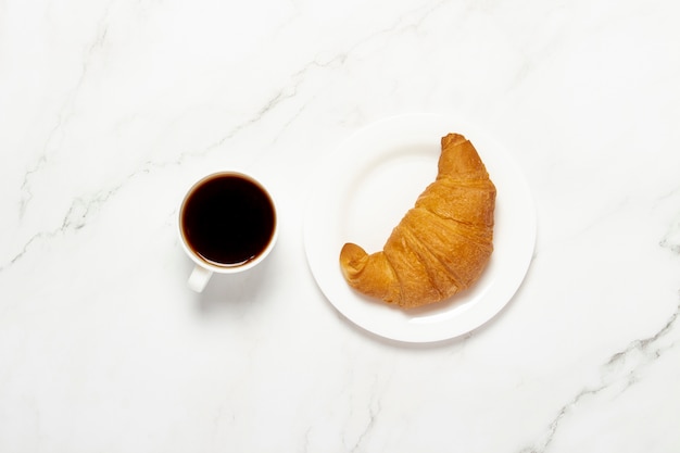 Tazza con caffè nero e croissant su un tavolo di marmo