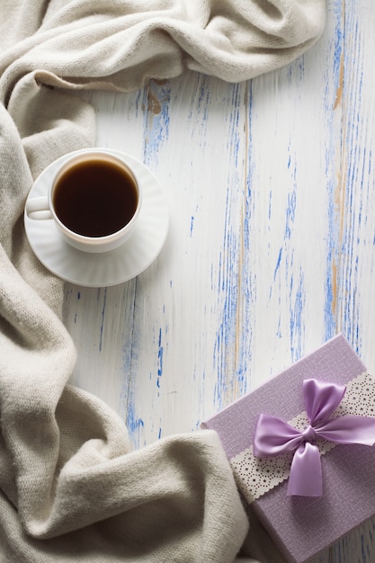 Tazza con caffè, sciarpa, regalo sul tavolo di legno bianco. Concetto di primavera