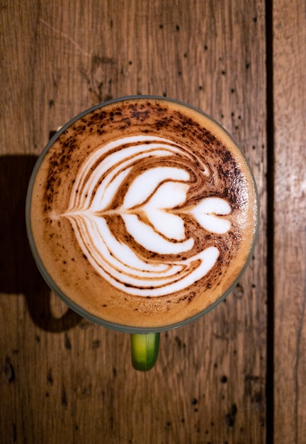 Tazza con cappuccino con schiuma di arte del latte a forma di cuore sul tavolo di legno nero al caffè. Una bevanda calda fumante alla caffeina sul piano portapaziente al bar.