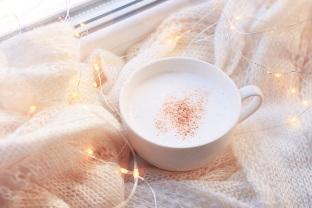 Tazza con cappuccino su una sciarpa calda alla luce delle luci