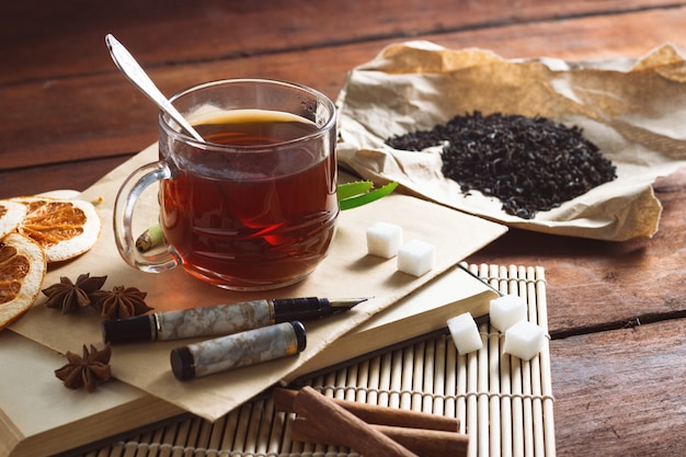 Tazza con tè, foglie di tè secche su carta artigianale, busta di zucchero fette e penna su un tavolo di legno