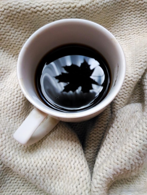 Tazza da caffè bianca con riflessione a foglia di cuneo nella tazza su sfondo beige lavorato a maglia