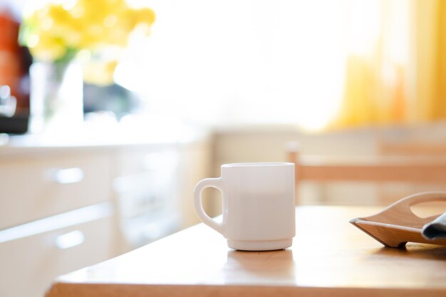 Tazza da caffè bianca con tovagliolo sul tavolo nell'interno della cucina reale con luce solare naturale brillante