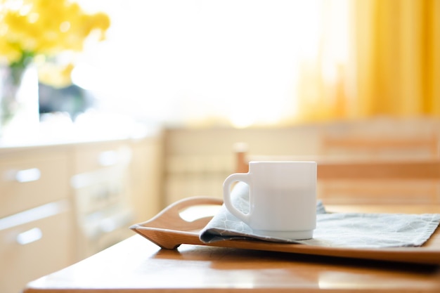 Tazza da caffè bianca con tovagliolo sul tavolo nell'interno della cucina reale con luce solare naturale brillante