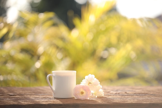 Tazza da caffè bianca e rose sulla tavola di legno all'aperto