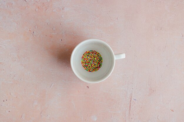 Tazza da caffè bianca piena di granelli di caramelle su uno sfondo di cemento invecchiato rosa.