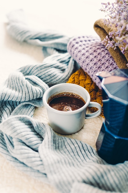 Tazza da caffè e caffettiera geyser blu su una coperta bianca, una pila di vestiti a maglia