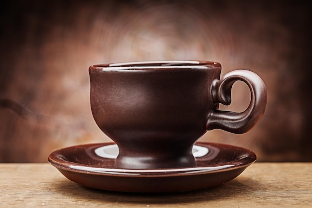 Tazza da caffè in argilla marrone sul piattino su sfondo di legno vintage