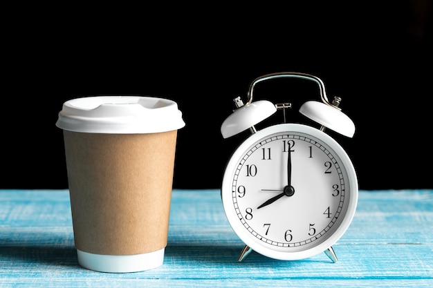 Tazza da caffè in cartone Tazza artigianale usa e getta e sveglia bianca su sfondo rustico Concetto di mattina in ufficio