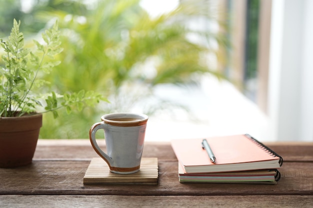 Tazza da caffè in ceramica vintage, quaderni e vaso per piante su tavolo di legno marrone