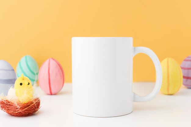 Tazza da caffè pasquale di colore bianco in piedi su un tavolo di legno con uova multicolori e un pollo