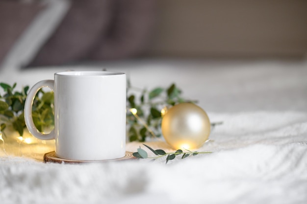 Tazza da caffè su uno sfondo a maglia beige con foglie di eucalipto e luci di ghirlande natalizie