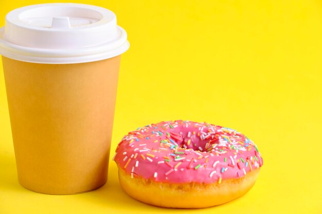 Tazza da caffè usa e getta e ciambella con sfondo giallo glassa rosa