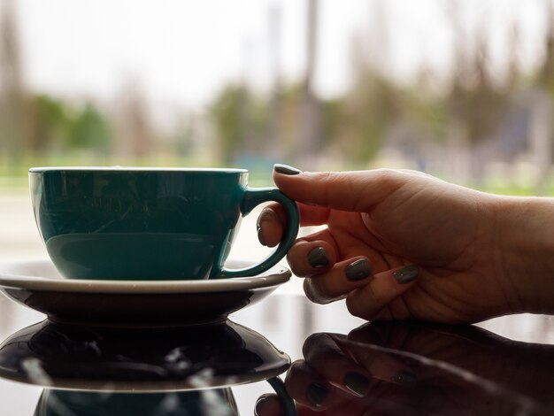 Tazza da caffè verde in una mano di donna