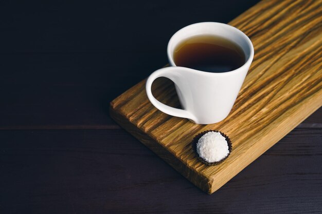 Tazza da tè bianca con cucchiaio e caramelle al cioccolato ed elefante nero sulla scrivania in legno