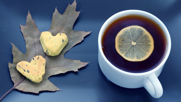 Tazza da tè bianca con limone su un piattino con biscotti e foglie d'autunno. dolce per merenda