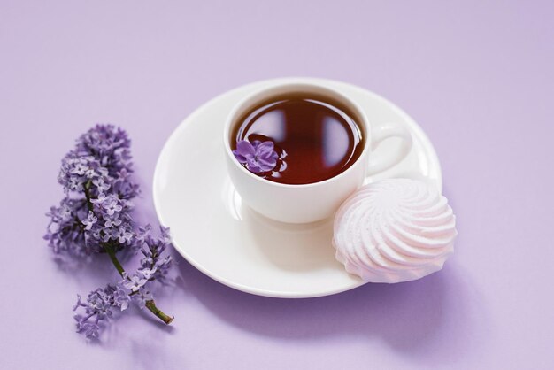 Tazza da tè con dessert marshmallow e fiori lilla su sfondo viola