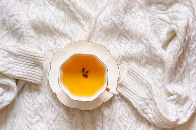 Tazza da tè in porcellana con bordo dorato su maglione lavorato a maglia bianco