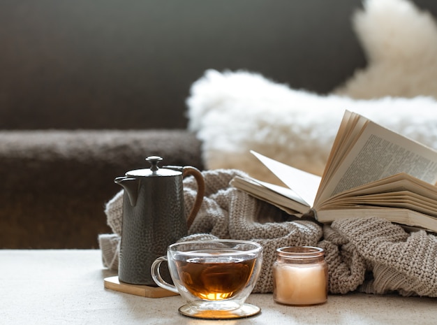 Tazza da tè in vetro, teiera e libro con elemento a maglia su sfondo sfocato. Il concetto di comfort e calore domestico.