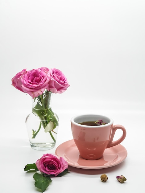 Tazza da tè rosa con rose in vaso di vetro su sfondo bianco