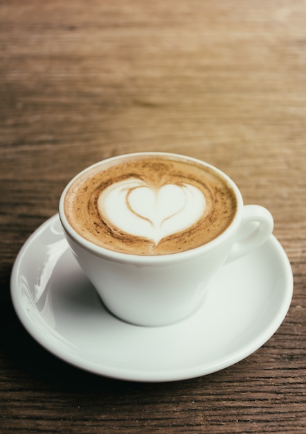 Tazza del caffè del cappuccino con arte di Latte di forma del cuore su fondo di legno