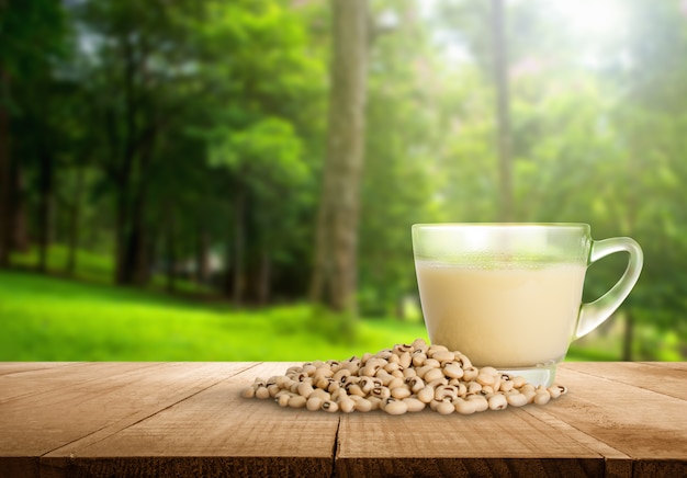 Tazza del latte di soia e fagiolo della soia con il fondo vago astratto della natura della foresta.