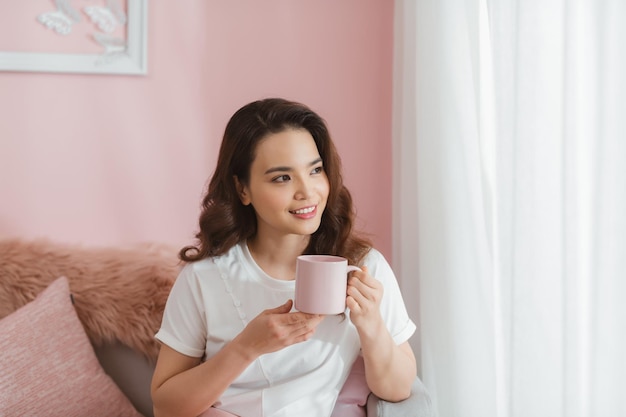 Tazza della holding della donna che sorride nella macchina fotografica nel salone