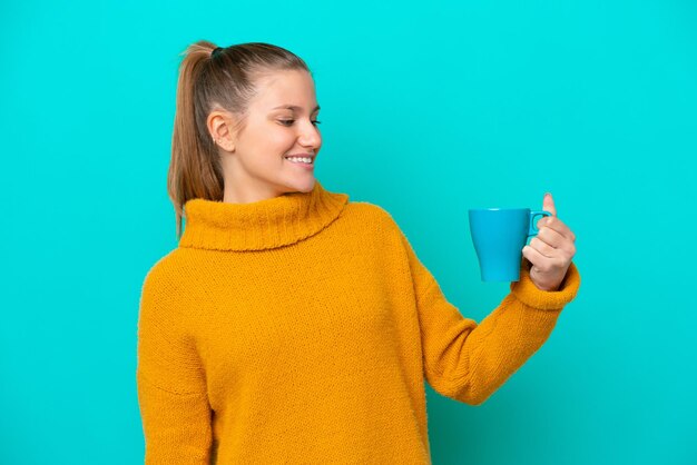 Tazza della holding della giovane donna caucasica isolata su fondo blu con l'espressione felice