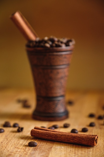 Tazza di argilla con chicchi di caffè e cannella su un tavolo di legno.