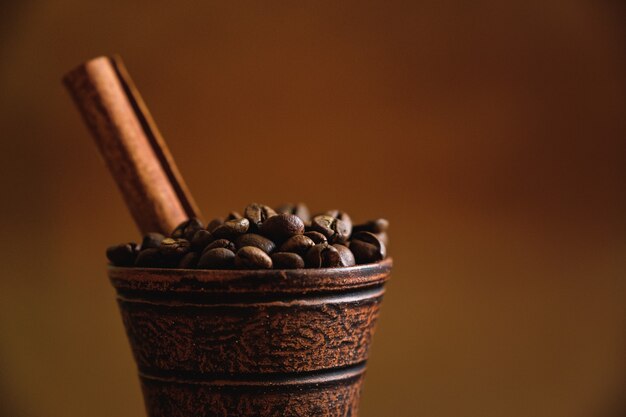 Tazza di argilla con chicchi di caffè e cannella su un tavolo di legno.