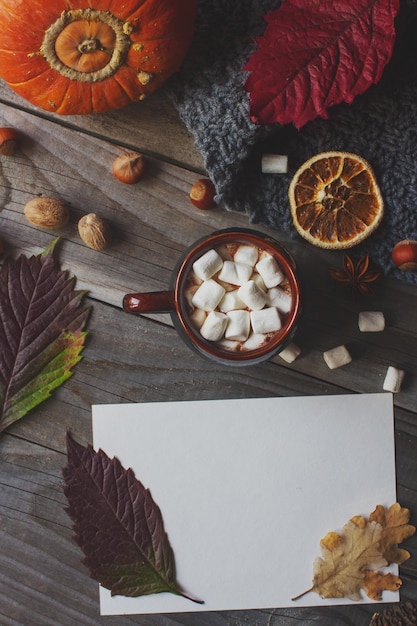 Tazza di cacao con marshmallow cartolina vuota foglie di zucca e noci su fondo di legno rustico accogliente caldo autunno foto vista dall'alto messa a fuoco selettiva tonica spazio per il testo