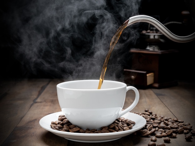 Tazza di caffè a vapore con macinino, beens, bollitore e tazza di vetro su sfondo scuro tavolo in legno grunge