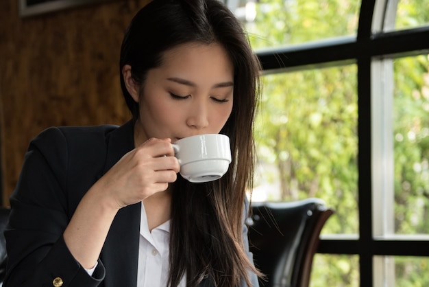 Tazza di caffè bevente della donna di affari di mattina al negozio.