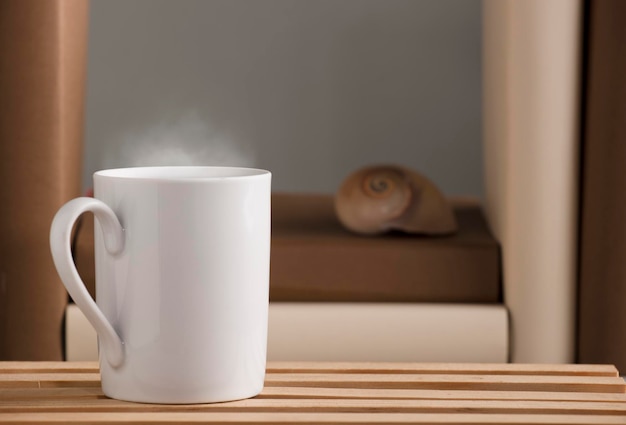 Tazza di caffè bianca con vapore caldo sulla scrivania con conchiglia nautilus e sfondo grigio di libri