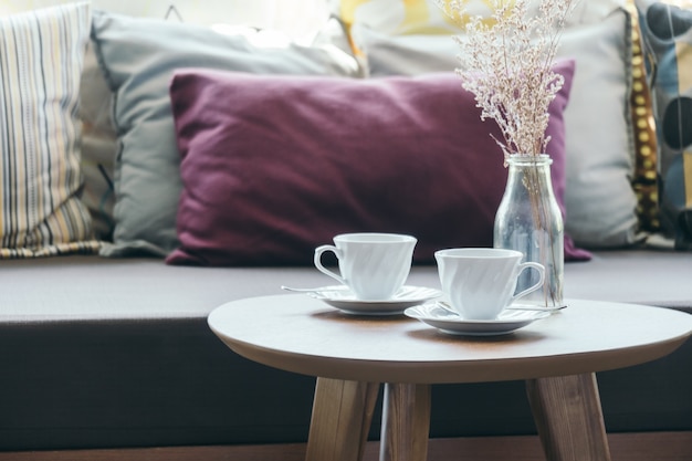 Tazza di caffè bianca con vaso di fiori sulla decorazione di tavolo con cuscino sul divano
