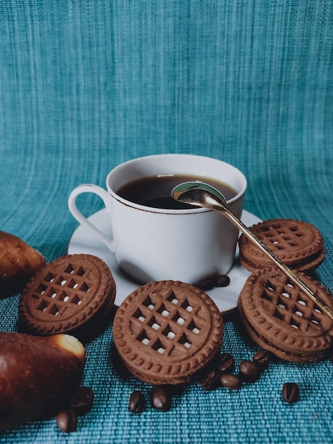 Tazza di caffè bianca e biscotti marroni rotondi su sfondo blu