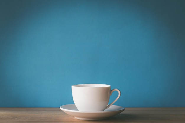 Tazza di caffè bianca sulla scrivania in legno con sfondo blu