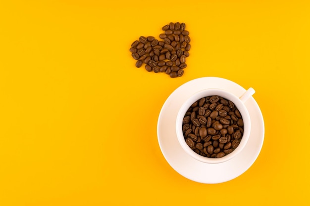 Tazza di caffè bianco con fagioli a forma di cuore Sfondo giallo Copia spazio