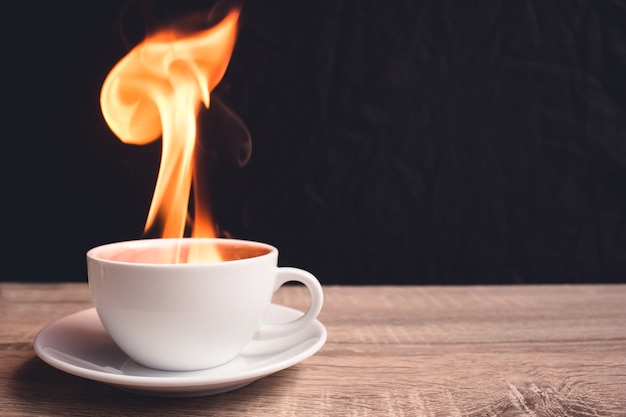 Tazza di caffè bianco con un fuoco all&#39;interno di un bicchiere è posto su un tavolo di legno