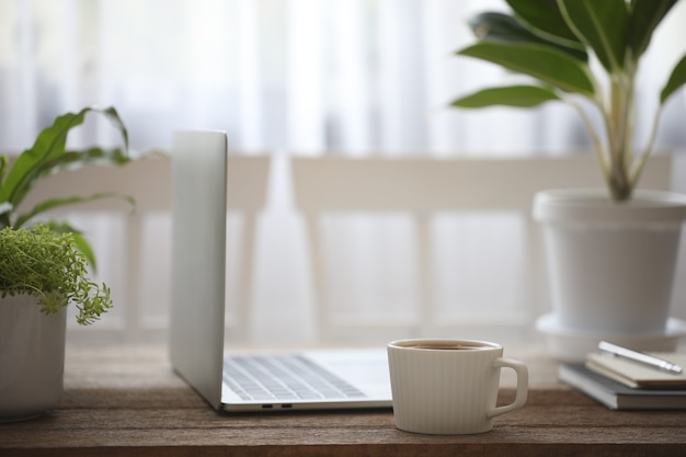 Tazza di caffè bianco e laptop e vasi per piante sul tavolo di legno marrone