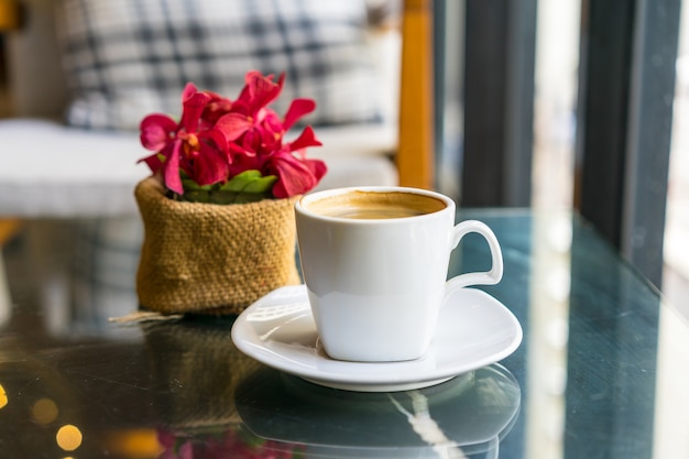 Tazza di caffè bianco sul tavolo e fiore sfocato