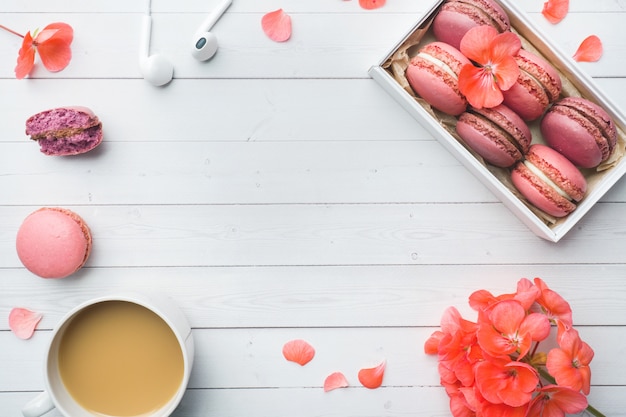 Tazza di caffè, biscotti del maccherone in una scatola, fiori con la disposizione piana